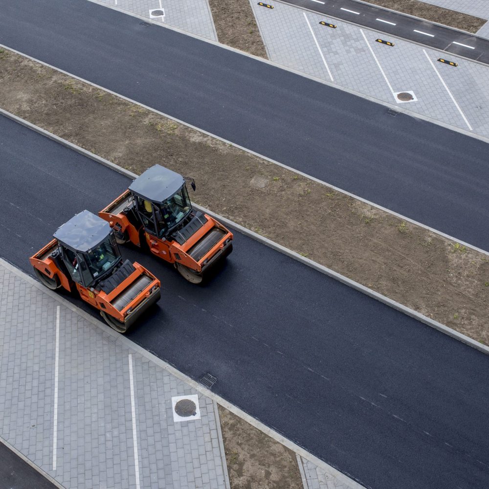 An aerial view of orange vibratory asphalt roller compactor on a new pavement